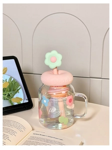 Close-up of a glass mug with pink silicone lid and flower straw in a cozy desk setting