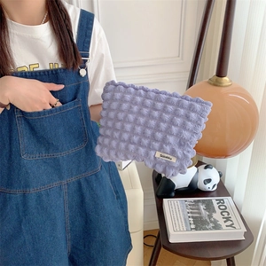 Close-up of a purple bubble textured fabric makeup bag held by a model in a home setting