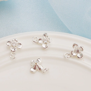 Close-up of four silver clover flower charms with zircon inlay for DIY jewelry making