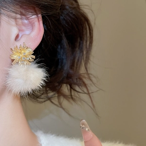 Close-up of gold fireworks studs with zircons and white pompom pendant on ear