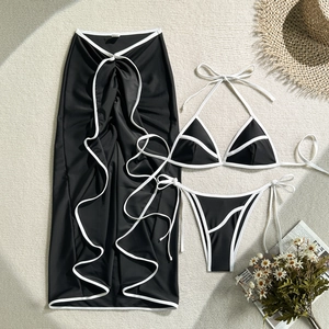 Detailed flat lay of black three-piece bikini set with white contrast piping and sarong skirt