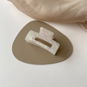 Detail of square acetate hair claw clip with iridescent white finish on silk