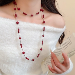 Detail of long pearl necklace with red beads and silver chain on a model in white