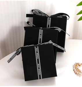 Three elegant square black jewelry gift boxes with Best Wishes ribbon on marble surface