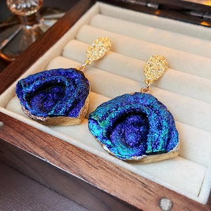 Close-up of blue crystal earrings with gold trim on a beige velvet jewelry box tray