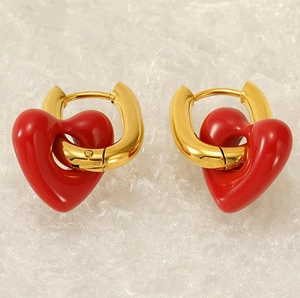 Close-up of gold-plated U-shaped earrings featuring red enamel heart-shaped charms