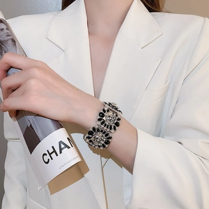 Detailed close-up of a floral black enamel bracelet on a wrist with white suit