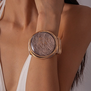 Close-up of a woven mixed-metal cuff bracelet with a large circular resin centerpiece
