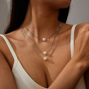 Detail of a triple-layered silver snake chain necklace with white pearl pendants