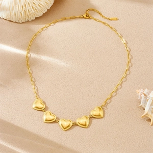 Gold-plated stainless steel necklace with five heart charms on a beach-themed background