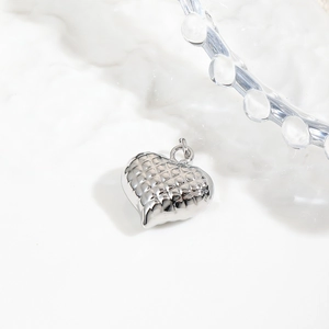 Macro shot of silver hollow heart pendant with quilted texture on white ceramic plate