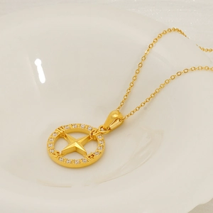 Gold stainless steel compass necklace with zirconia inlays on a white ceramic tray