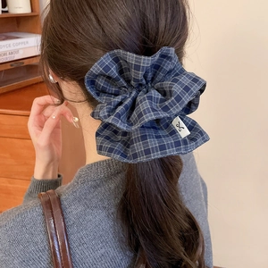 Blue-gray checkered fabric scrunchie shown in a stylish low ponytail hair accessory look