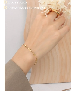 Détail d'un bracelet en croix plaqué or 18K et bague carrée sur fond de bois