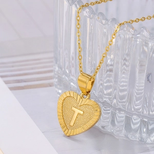 Detail of heart-shaped gold pendant with letter T on a textured matte finish surface