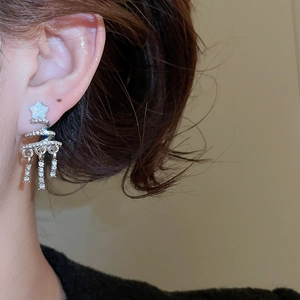Close-up of silver spiral star earrings with zircon tassels on a model's ear