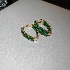 Macro shot of gold hoop earrings with rectangular green zircon stones on silver background