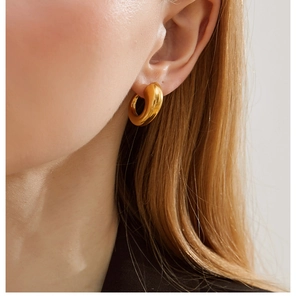 Close-up of a minimalist chunky gold hoop earring worn by a model in 18K gold-plated steel