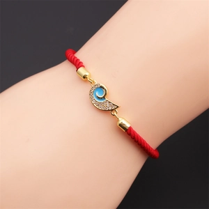 Macro shot of red braided rope bracelet with blue enamel and gold zircon pendant on wrist