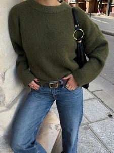 Olive green knitted long sleeve sweater paired with blue jeans in an urban street setting