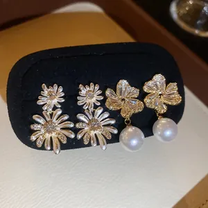 Elegant floral pearl earrings with zircon inlay and enamel finish on a black display stand