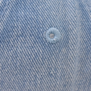 Macro shot of embroidered ventilation eyelets on washed denim baseball cap texture