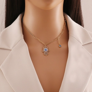 Gold Hamsa Hand necklace with blue Evil Eye pendant worn by a model in a beige suit