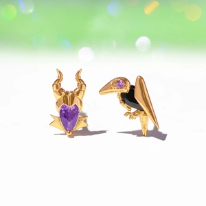 Detailed close-up of asymmetric gold villain earrings with purple zircon and raven motif