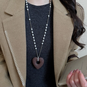 Detailed view of large textured heart pendant on long pearl and silver chain necklace