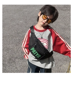 Outdoor street shot of kids black chest bag with green letters worn by a child