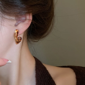 Close-up of leopard print resin J-hoop earring worn by a model in warm lighting