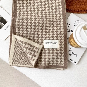 Close-up of houndstooth knit scarf with brand label, coffee cup and lifestyle props