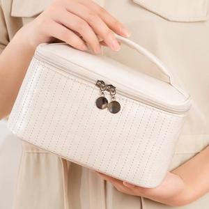 Portable white PU leather makeup bag with dot texture and dual zippers held by a model