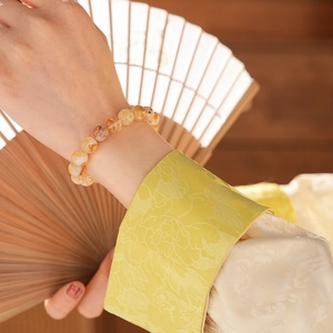 Gros plan d'un bracelet en perles de citrine au poignet avec fond en soie et éventail