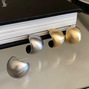 Macro di orecchini a C in oro e argento satinato opaco fissati su una pagina di libro