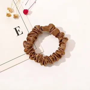 Detail of a brown satin scrunchie showing glossy pleated texture and elastic material