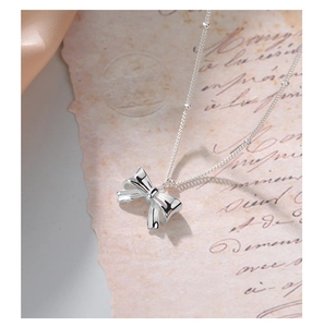Close-up of S925 sterling silver bow necklace with elegant beaded chain on vintage paper