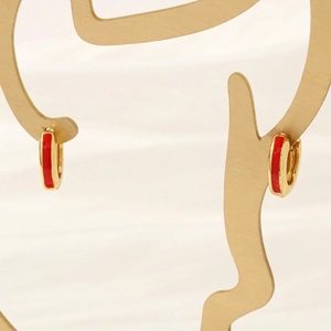 Macro view of 18K gold plated hoop earrings with red enamel on a decorative stand