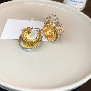 Close-up of chunky gold and silver textured hoop earrings with a crumpled metal finish