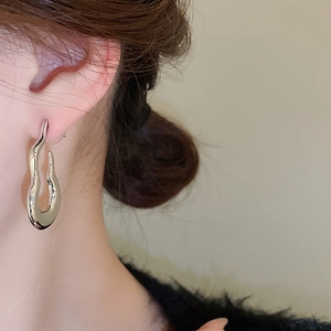 Close-up of liquid metal style wavy silver stud earrings worn on a model's ear