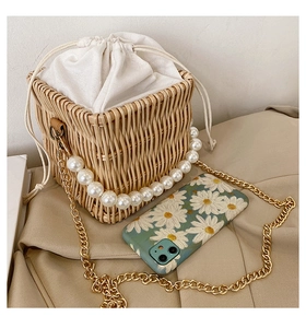 Close-up of handwoven straw bucket bag with white faux pearl handle and gold chain strap