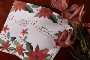 Close-up of gold foil Christmas cards with red poinsettia and pine cone motifs