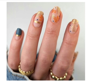 Detail of short press-on nails with green plant prints, matte navy, and gold foil accents