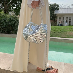 Detail of silver sequin tote bag with metallic chain strap held by model in outdoor setting
