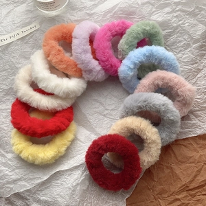 Twelve colorful fuzzy faux rabbit fur scrunchies arranged on a textured white background