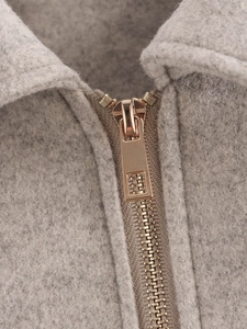 Detailaufnahme eines goldenen Metallreißverschlusses an einer hellgrauen Tweedjacke
