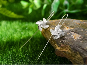 Macro shot of S925 sterling silver windmill drop earrings against natural green grass background