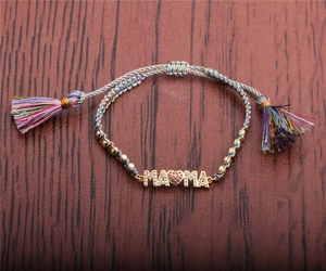 Detail of colorful woven bracelet with gold MAMA charm and ruby heart pendant