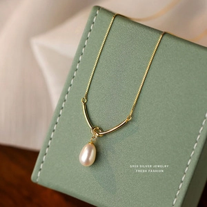 Macro view of S925 silver golden necklace with a teardrop pearl on a green box