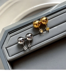 Detailed view of polished gold and silver ball stud earrings on a grey velvet tray